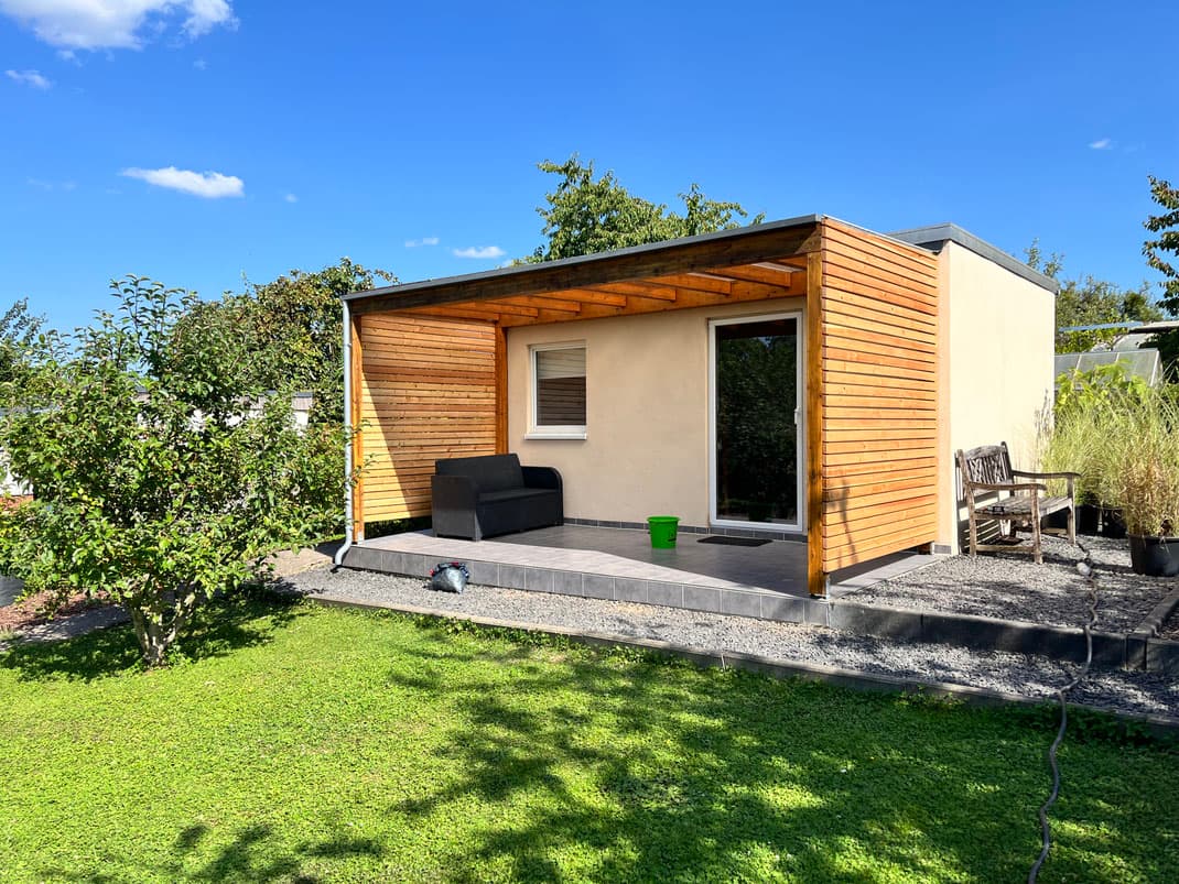 Gartenhaus mit Holzverkleidung und integrierter Terrassenüberdachung im Sommer.