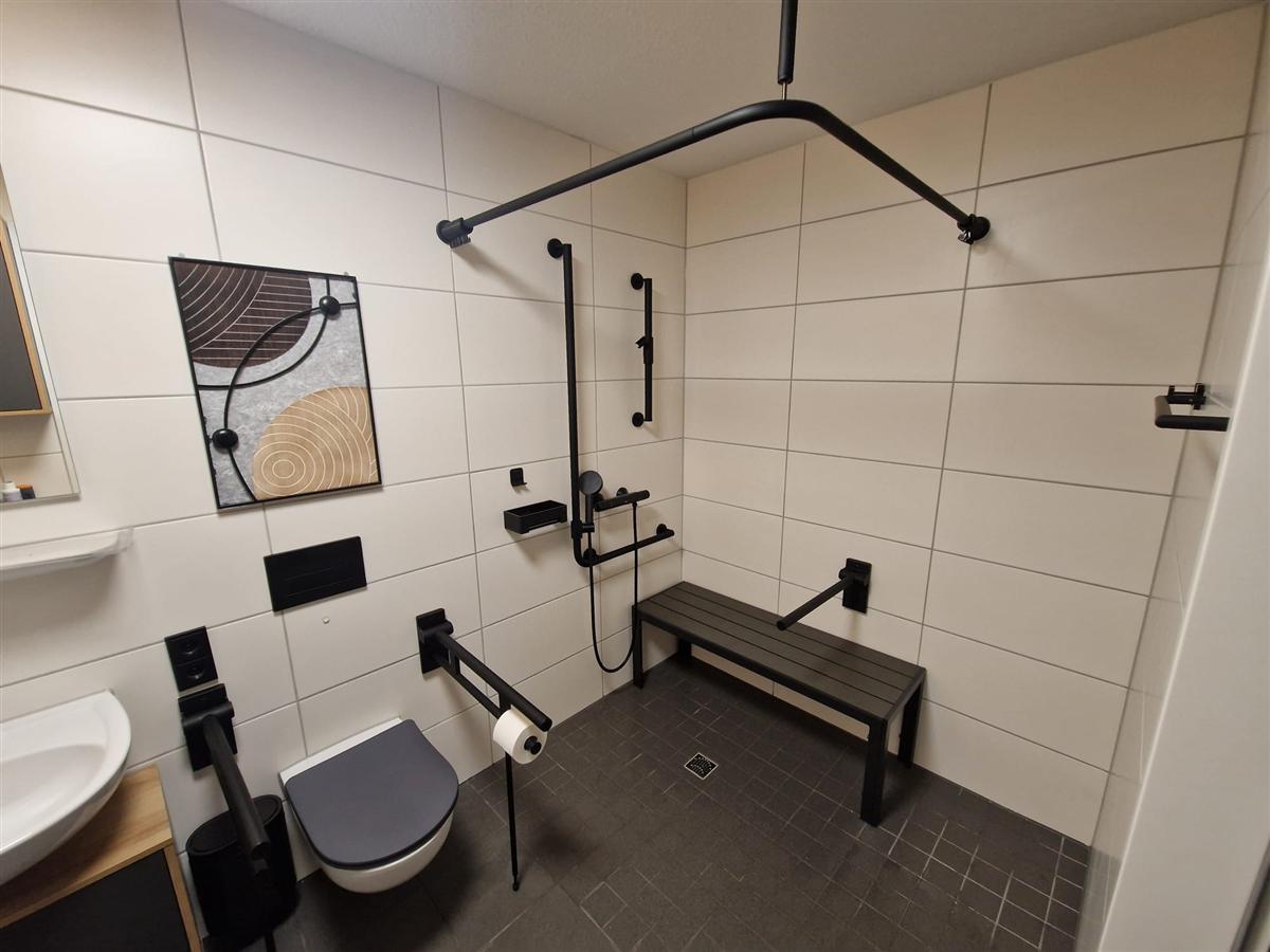 Barrierefreies Bad komplett ausgebaut, schwarze Haltegriffe und Duschstange fachgerecht montiert.