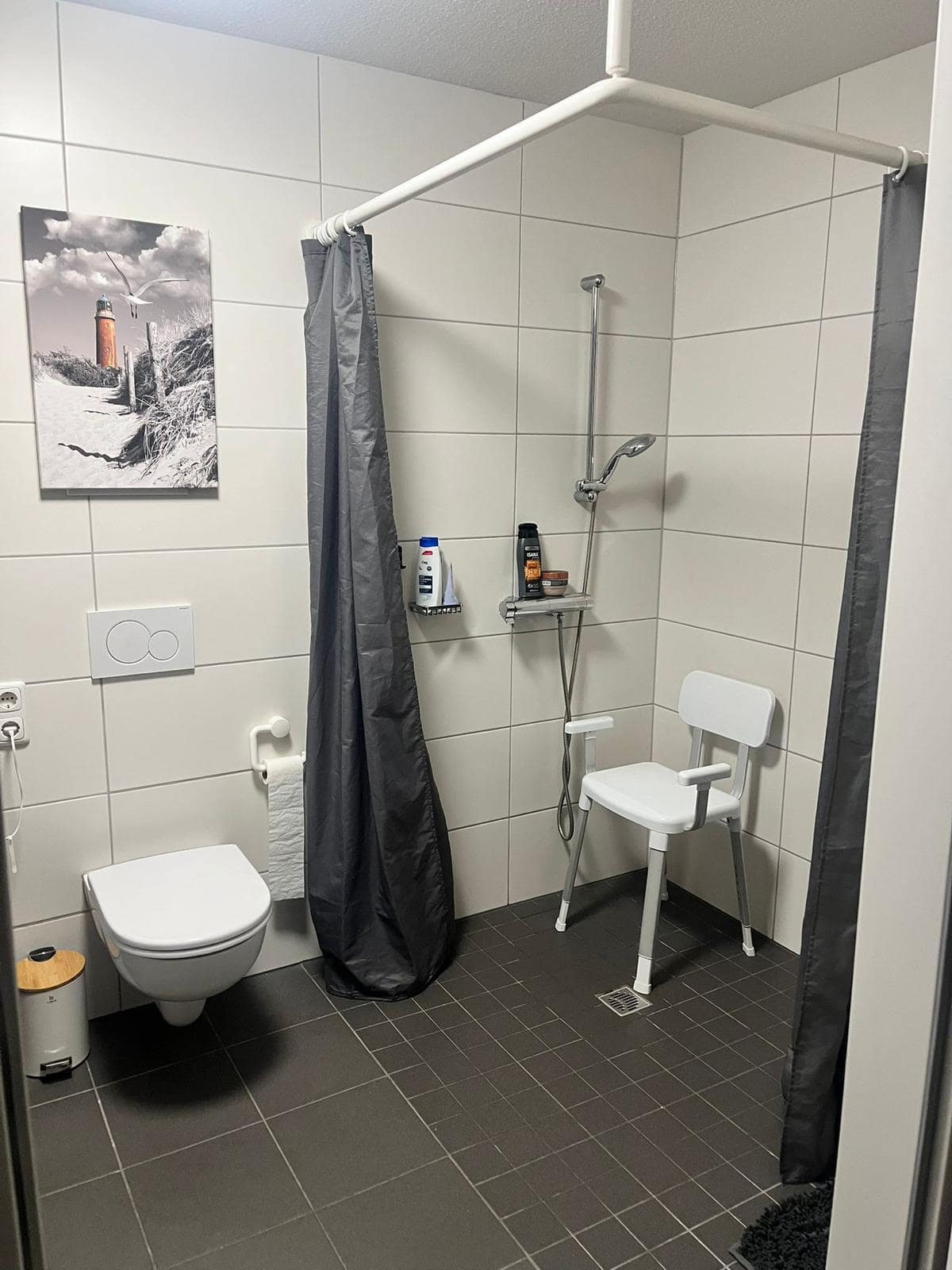 Barrierefreie Dusche mit weißen Haltegriffen und Duschstuhl, sauber montiert.