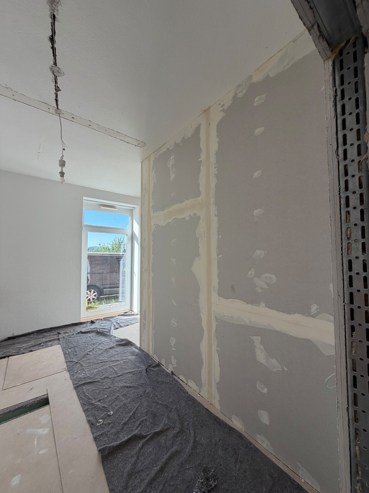 Neu errichtete Trockenbauwand mit verspachtelten Plattenstößen in hellem Raum, Blick zur Fenstertür.