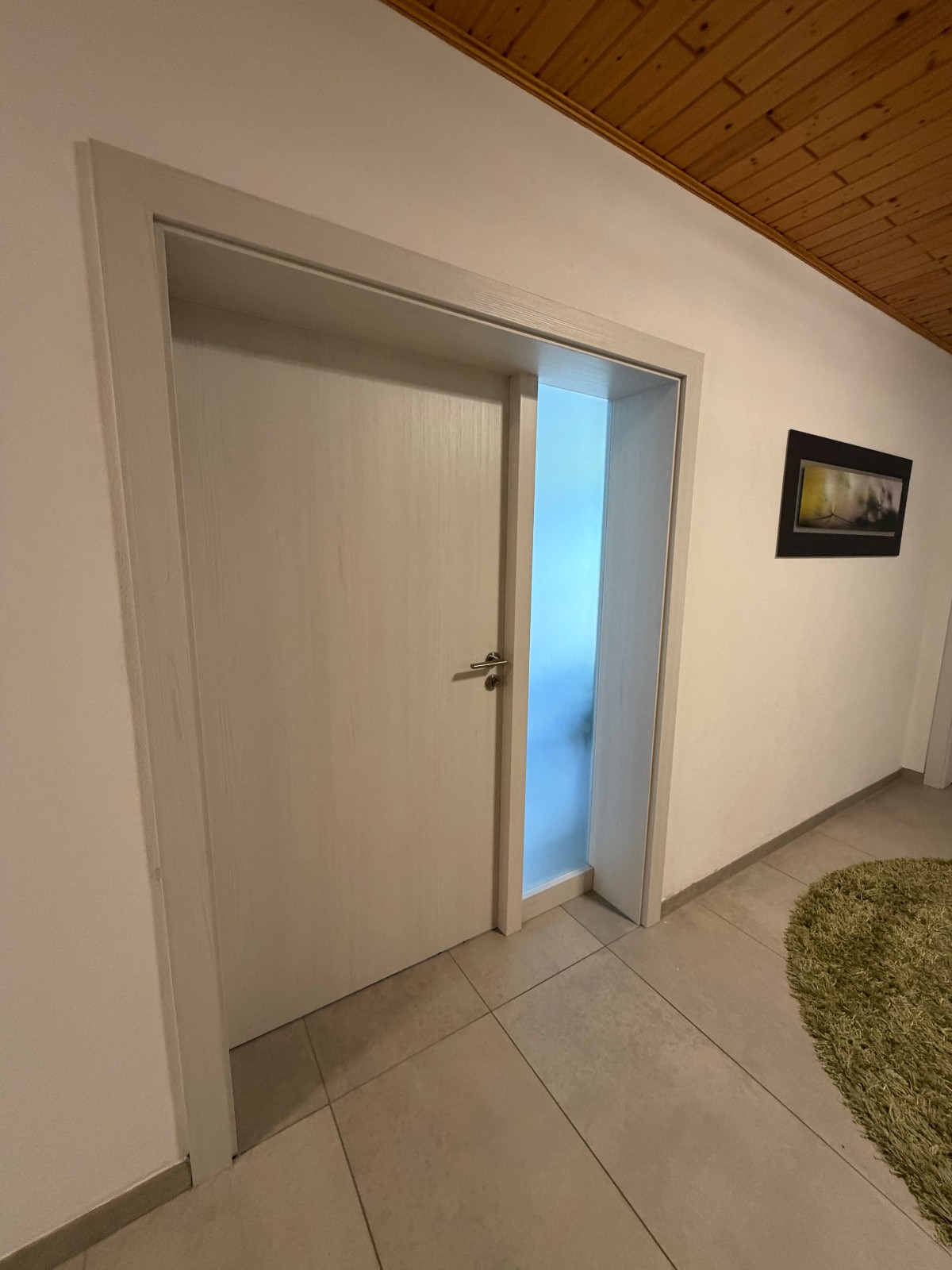 Montierte weiße Innentür mit satiniertem Glas-Seitenteil im Flur mit Holzdecke und Fliesenboden.