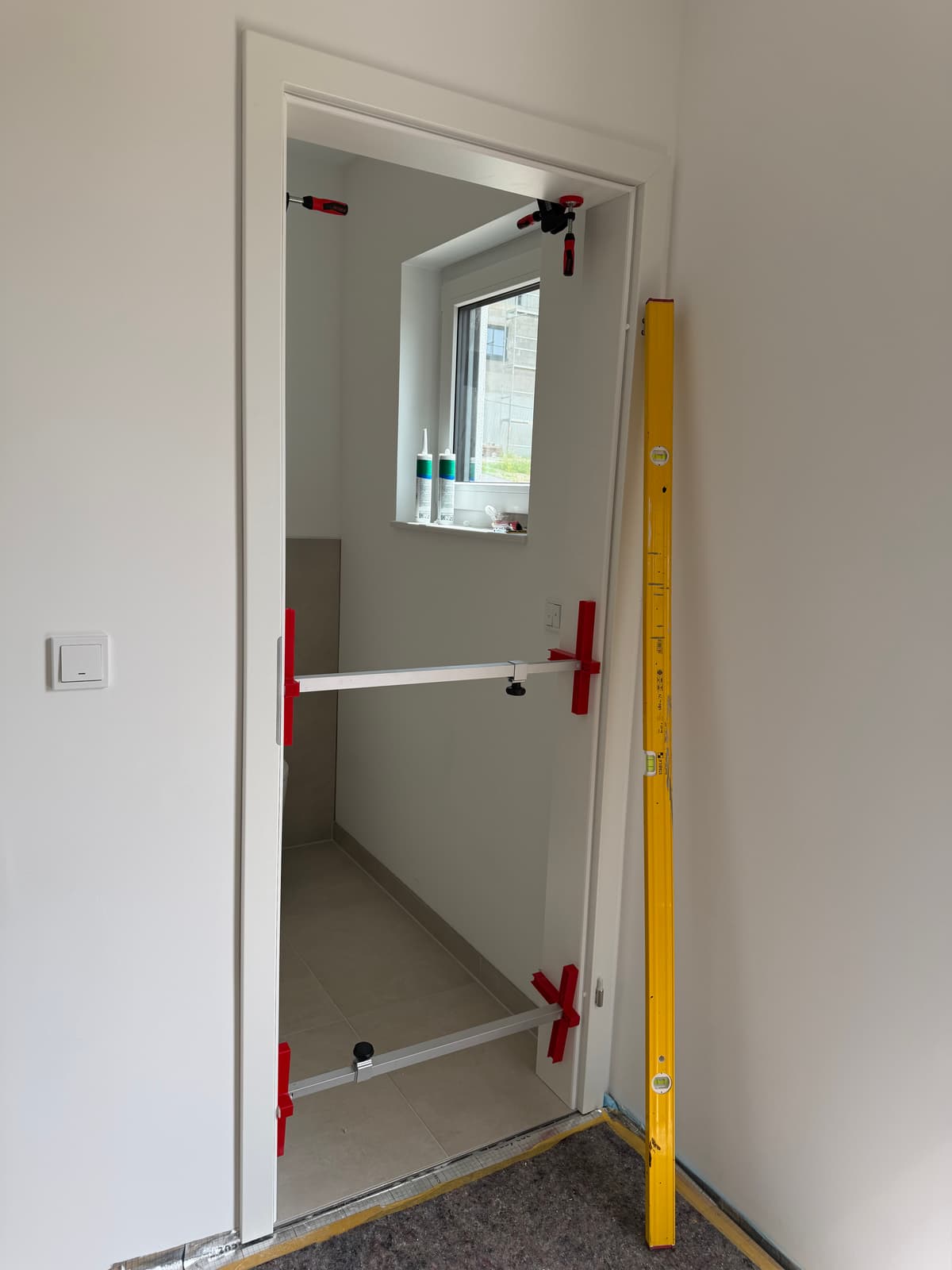Türzarge im Einbau, fixiert mit Zargenspannern und Wasserwaage, Blick durch den Türrahmen in Badezimmer.